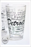 Pint Glass featuring Detroit, Michigan with highlights from the town in black screen print.