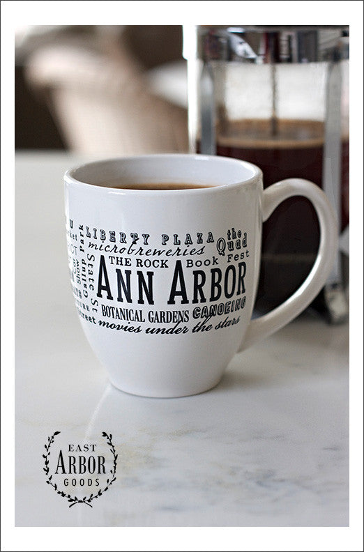 White ceramic coffee mug featuring Ann Arbor, Michigan with places and activities featured in different fonts in black screen print. 