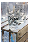 A group of pint glasses on a wood crate with one main one in focus featuring Detroit, Michigan with highlights from the town in black screen print.