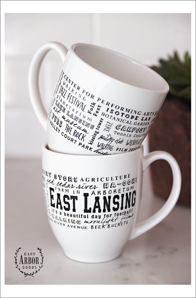 White ceramic coffee mug featuring East Lansing, Michigan with places and activities featured in different fonts in black screen print.  
