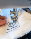 Close up of brand tag from East Arbor Goods being sewn onto the white linen of the pillow. Tag says "Made in Michigan." 
