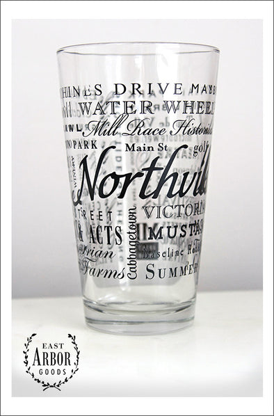 Pint Glass featuring Northville, Michigan with the word Northville in large script in the middle and words of places and activities in different fonts and sizes surrounding. All of the words in black screen print. 