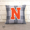 Gray and white large checked accent pillow with a large orange "N" varsity letter sitting on a cement countertop and leaning against a white brick background. 