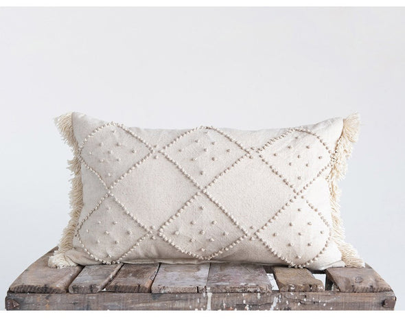 Cream pillow on wood crate. Cream cotton-linen pillow with designs of diamonds made from cream thread dots. The two sides of the pillow have fringe detail with cream thread. 