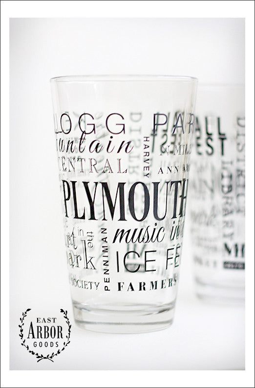 Two pint glasses with one in the center and main focus to show the black screen print details of words in different fonts and sizes featuring highlights of places and activities in Plymouth, Michigan.