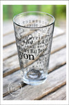 Right side view of Pint Glass featuring South Lyon, Michigan with highlights from the town in black screen print. On an outdoor wood plank table with green grass in the background.