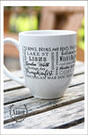 Close up of the back of a large white ceramic mug on an outdoor wood table with trees in background. Design on mug wraps around the middle of the mug with words in different sizes and fonts around the main words "South Lyon." Each word related to the town.