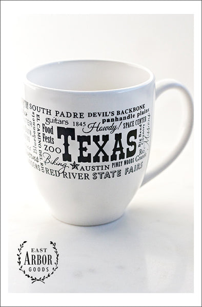 White ceramic coffee mug featuring Texas with a black screen print design of words in different fonts and sizes around the word Texas.  Mug on a white background. 