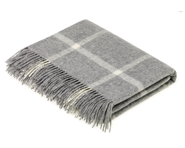 Merino wool throw folded on a white background. Throw is a white and gray wool throw with a classic windowpane design and gray and white tassels on the edges. 