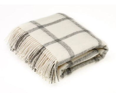 Folded wool blanket throw with cream and black large lattice design. Edge of blanket has tassels in the same colors. 